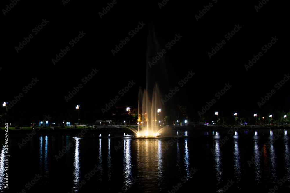 View cityscape Udonthani city and landscape fountain spray in pond night time for thai people travel visit and rest relax at Nong Prajak Recreation Centre Public Park in Udon Thani, Thailand