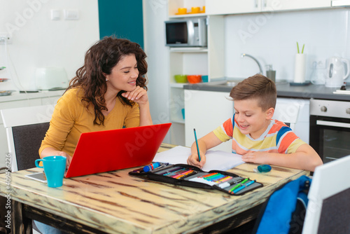 Smiling mother helping adorable son doing schoolwork at home