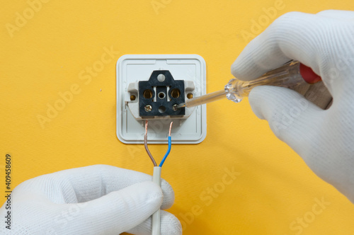 an electrician in white gloves screws wires to an electrical outlet on a yellow wall, top view, close-up photo