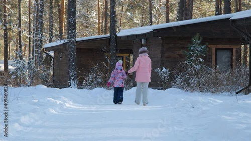 Little Girl with her Mother Walking Between Conifer Trees in Sunny Frosty Winter Day. Back View. Harmony with Nature, Leisure, Winter Family Activities, People and Lifestyle Concept photo