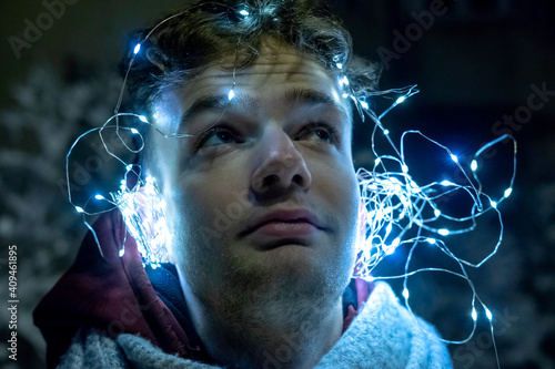 Obraz na płótnie A young handsome unshaven guy with a garland on his head, crested on his ears like headphones. New Year and Christmas music concept w salonie