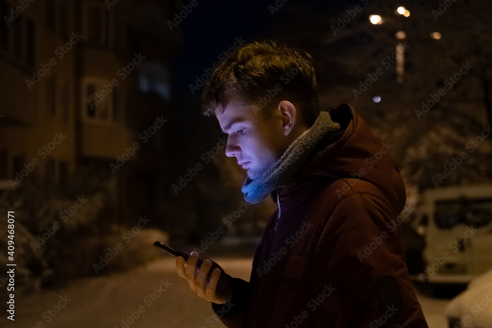 a young man, a guy holding a mobile phone in his hands on a winter evening on the street