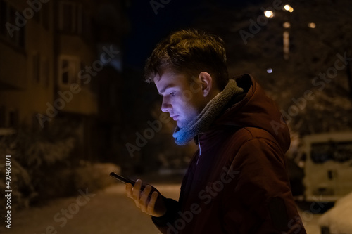 Obraz na płótnie a young man, a guy holding a mobile phone in his hands on a winter evening on the street w salonie
