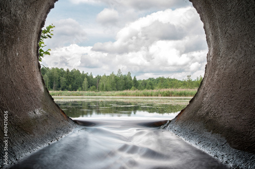Perfect view from concrete drain pipe in the forest river. Beautiful water flow from the lake.