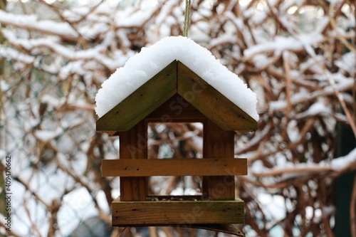 small wooden bird house full of snow is hanging at  a tree in the garden © Bianca