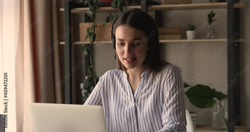 Smiling young business lady wearing wireless headset with microphone, holding video call web camera meeting with partners or discussing working issues with colleagues distantly at home office. Smiling young business lady wearing wireless headset with microphone, holding video call web camera meeting with partners or discussing working issues with colleagues distantly at home office.