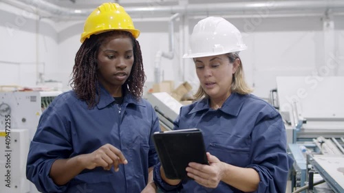 Middle aged female engineer showing machines and equipment work on plant floor to black new employee. Dolly shot. Industrial occupation concept