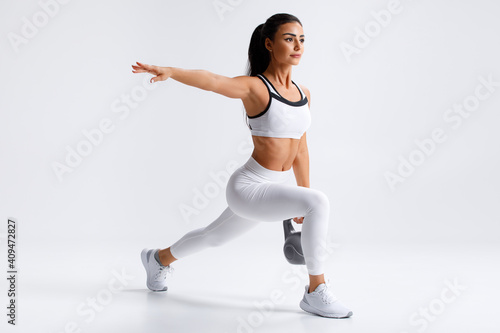 Fototapeta Naklejka Na Ścianę i Meble -  Fitness woman doing lunges exercises with kettlebell, leg muscle training. Active girl doing front forward one leg step lunge