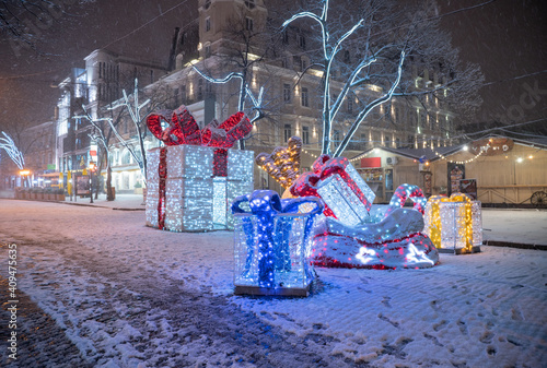 Festive decor in the form of gifts with ribbons and illuminated lights on the European street of the night city. Romantic atmosphere  © Liudmyla