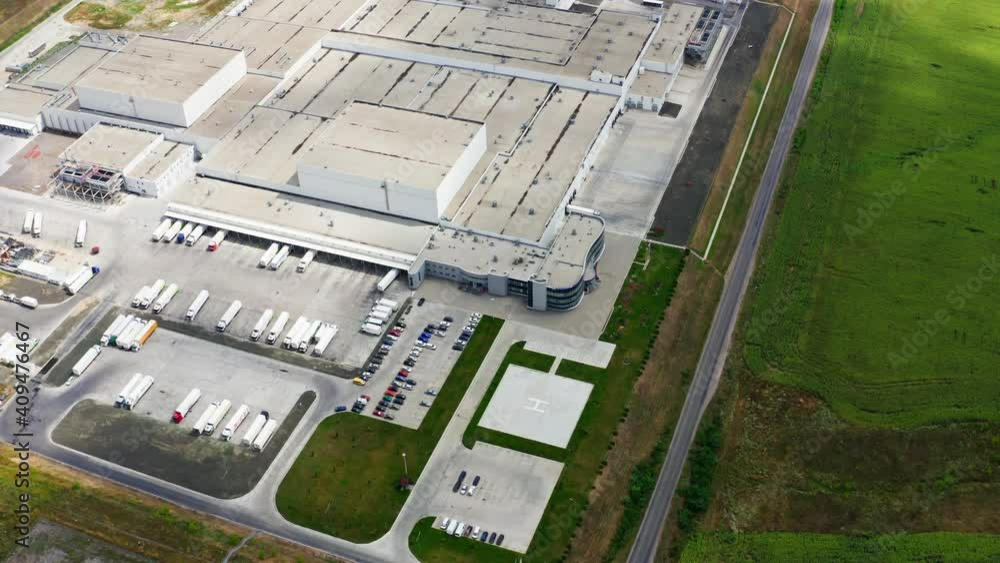 Industry on green field. Trucks and cars near the modern factory. Roofs of a large industrial plant with car parking. Aerial view. Industry on green field. Trucks and cars near the modern factory. Roofs of a large industrial plant with car parking. Aerial view.