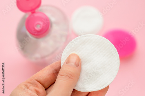 Female hand holding a cotton pad, micellar water with cotton disks on pink background. Beauty skin care concept photo