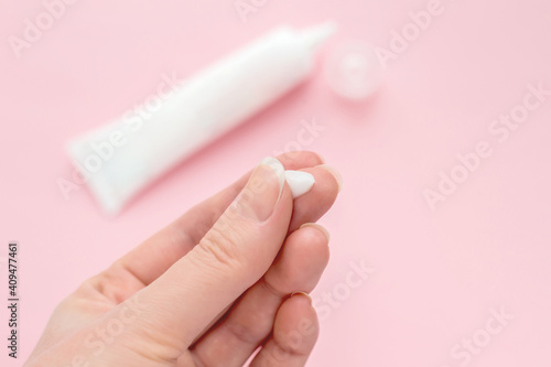 Female hand with a drop of cream on a finger. tube of cream isolated on a pink background. Antibacterial acne cream for problem skin. Сream to reduce pore tightening, anti-wrinkle eye cream