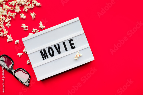 Popcorn, 3D glasses and lightbox text Movie time on red paper background. Top view Template