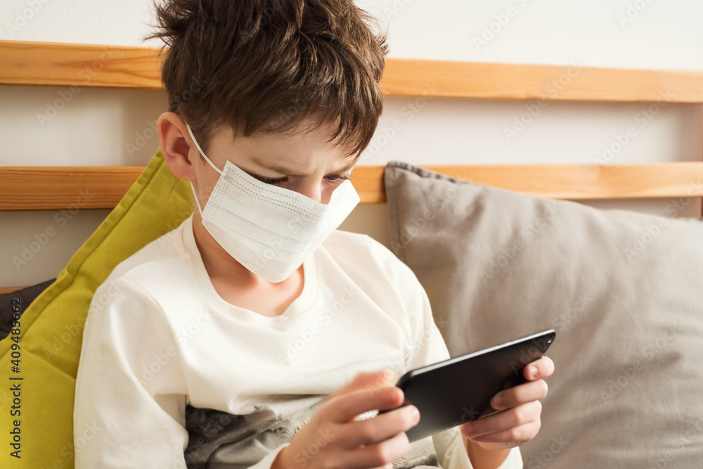 Boy medical mask is watching school lesson tablet, sitting bed on