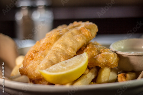 Classic crispy deep fried fish and chips with lemon and tartar sauce white dish on a wooden table