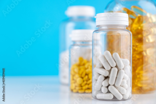 White gel capsules scattered on white surface. Orange pills in bottle blue background. Nutritional Supplements, Vitamins. Omega 3, multivitamins, Calcium, antibiotics. Health. Immunity