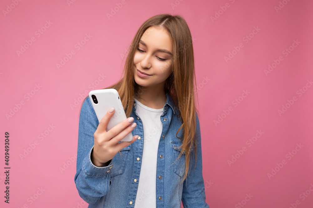 Beautiful young woman wearing casual clothes standing isolated over background surfing on the internet via phone looking at mobile screen Beautiful young woman wearing casual clothes standing isolated over background surfing on the internet via phone looking at mobile screen