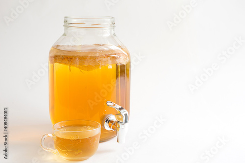 Kombucha-a drink made from tea mushroom in a glass jar with a tap. Transparent mug with a yeast drink made from a Japanese mushroom-jellyfish. White background, healthy food. Copy space