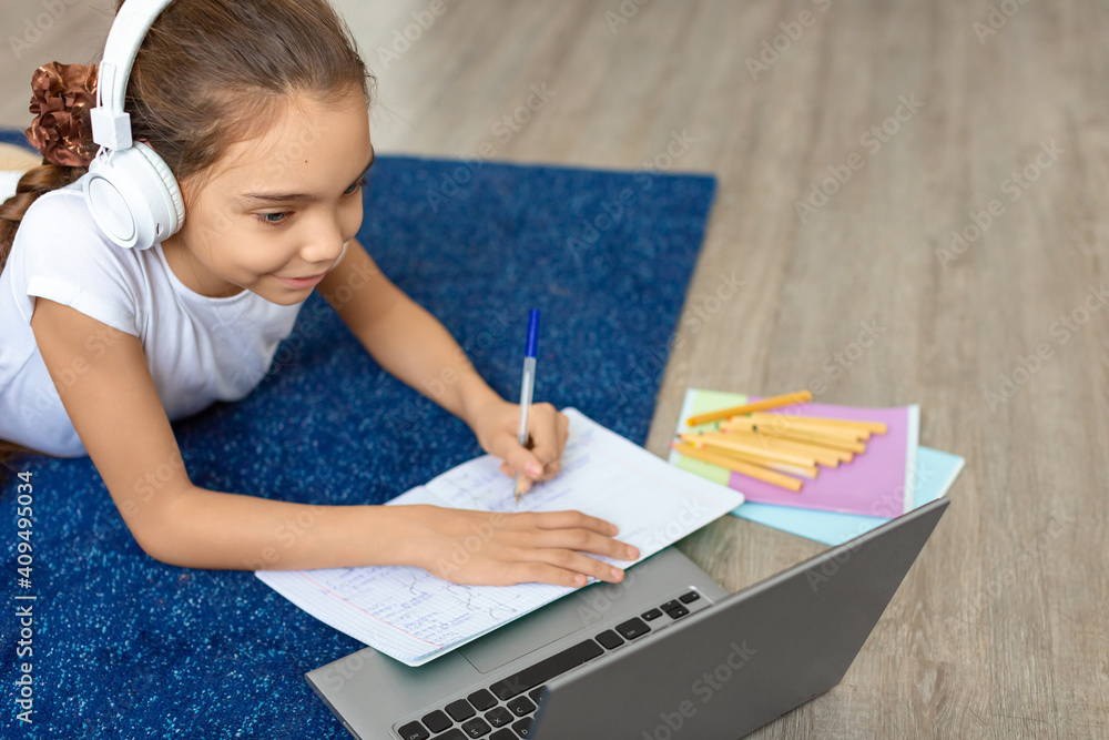 Photo of a pupil girl doing homework on the floor at home in front of a laptop monitor. Photo of a pupil girl doing homework on the floor at home in front of a laptop monitor.