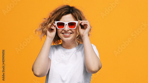 Portrait of happy pretty woman stylish white sunglasses with red glasses raises up, smiling with pleasure on yellow background in summer. Emotions. Positive girl. Lifestyle. Freedom © marina_larina