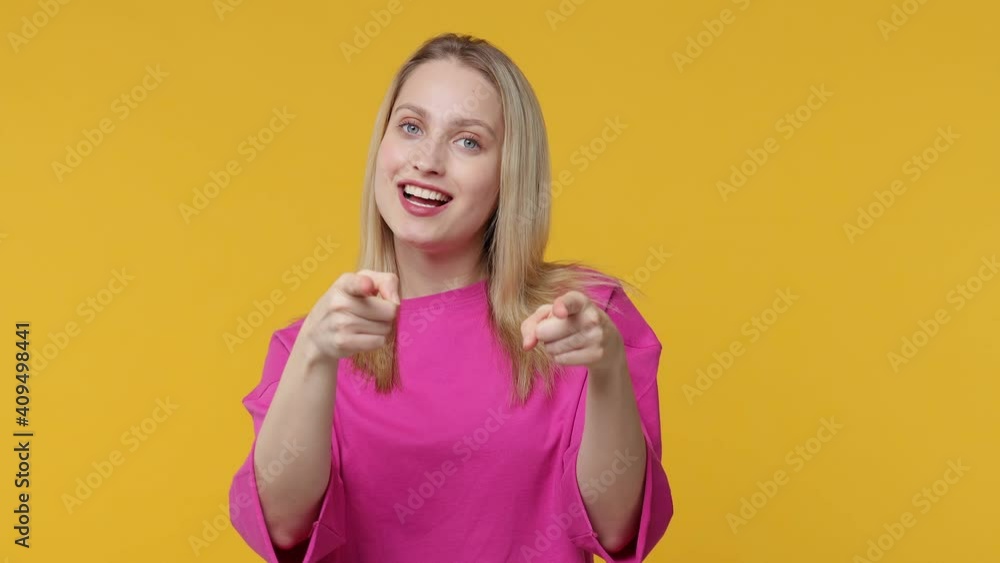 Cheerful funny young woman in pink t-shirt isolated on yellow background studio. People lifestyle concept. Point fingers camera on you showing thumbs up like gesture blinking blowing sending air kiss Cheerful funny young woman in pink t-shirt isolated on yellow background studio. People lifestyle concept. Point fingers camera on you showing thumbs up like gesture blinking blowing sending air kiss