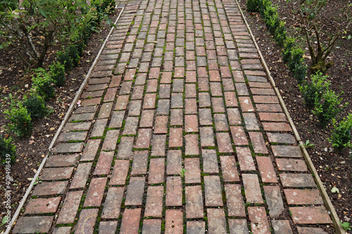 A pathway made from old bricks runs between flower beds with newly planted shrubs