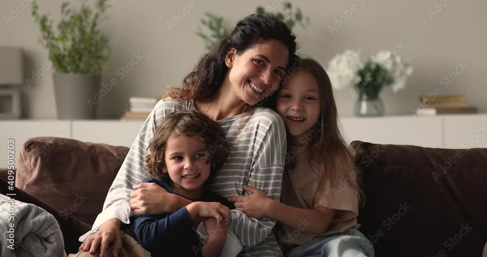 Loving mother her little son and 6s daughter family portrait concept. Preschool girl and boy hugging beautiful young 35s mommy sitting together on couch in living room at home smiling look at camera Loving mother her little son and 6s daughter family portrait concept. Preschool girl and boy hugging beautiful young 35s mommy sitting together on couch in living room at home smiling look at camera