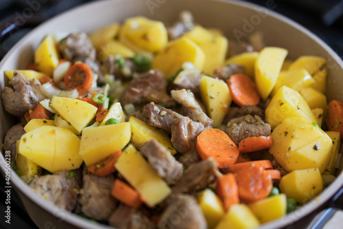 Meat stewed with potatoes, carrots, vegetables and spices in a pan. Process of cooking dish in a kitchen. Selective focus with copy space