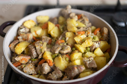 Meat stewed with potatoes, carrots, vegetables and spices in a pan. Process of cooking dish in a kitchen. Selective focus with copy space