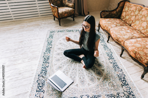 Beautiful brunette fitness woman make stretching exercises in front laptop, doing yoga indoors at home. Staying fit and healthy photo