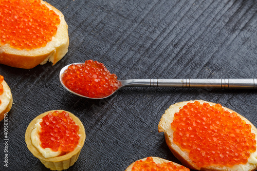 Toast with butter and red caviar and a spoon with caviar on a black board on a concrete background.