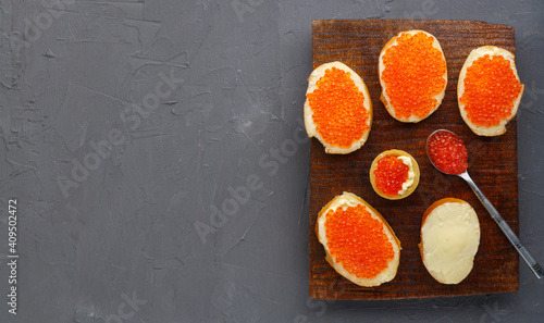 Canapes with butter and red caviar and a tartlet and a spoon with caviar on a brown board on a concrete background copy space