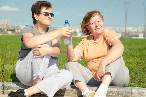 Two pensioner woman resting after training in the park. Fitness training for aged people. Healthy lifestyle concept.