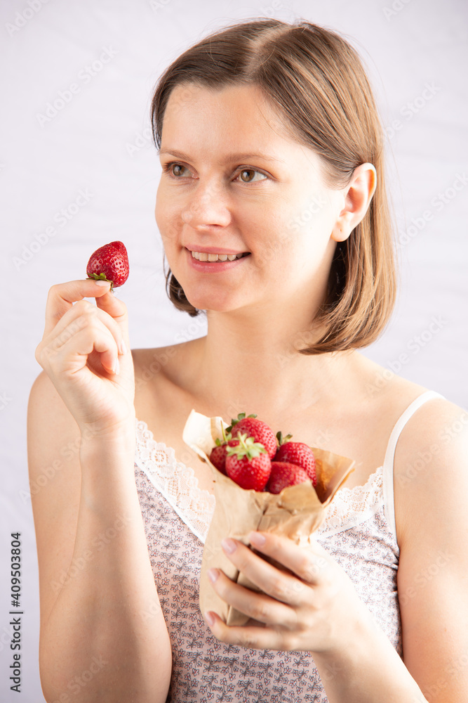 Young healthy good looking woman eats a ripe strawberry, the concept of a healthy lifestyle with organic products and vitamins. Attractive caucasian female with a happy expression. Young healthy good looking woman eats a ripe strawberry, the concept of a healthy lifestyle with organic products and vitamins. Attractive caucasian female with a happy expression.