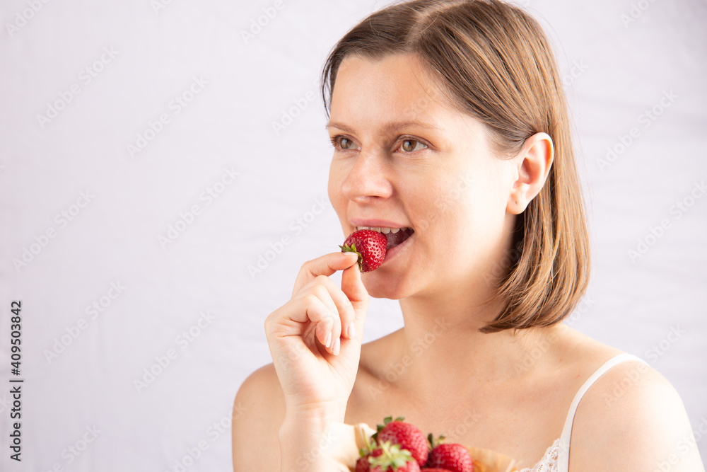 Young healthy good looking woman eats a ripe strawberry, the concept of a healthy lifestyle with organic products and vitamins. Attractive caucasian female with a happy expression. Young healthy good looking woman eats a ripe strawberry, the concept of a healthy lifestyle with organic products and vitamins. Attractive caucasian female with a happy expression.