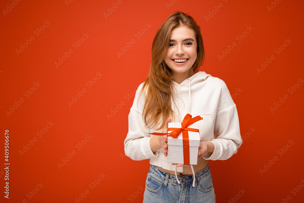 Beautiful happy young blonde woman isolated over colourful background wall wearing stylish casual clothes holding gift box and looking at camera Beautiful happy young blonde woman isolated over colourful background wall wearing stylish casual clothes holding gift box and looking at camera