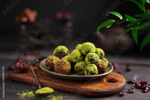Matcha energy sweets balls made of dried fruits dusted with bright green matcha powder on rustic wooden table, dark background. Raw vegan healthy candies - dessert. Copy space.