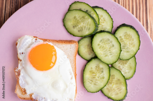toast with egg on a plate. Fresh cucumbers. slice of white bread on a pink background. sandwich. breakfast with fried egg. High quality photo
