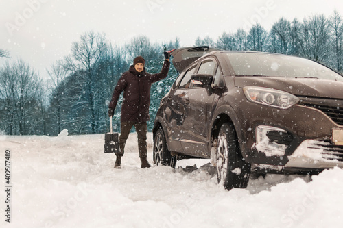 A man takes a shovel from a car stuck in the snow outside the city. Snowy. Transportation, vehicle stuck in the snow. concept.