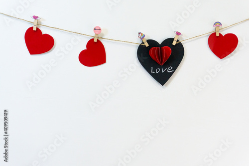 A black chalk heart with the inscription love and red hearts hang on a rope on a white background for Valentine's Day. Copyspace.