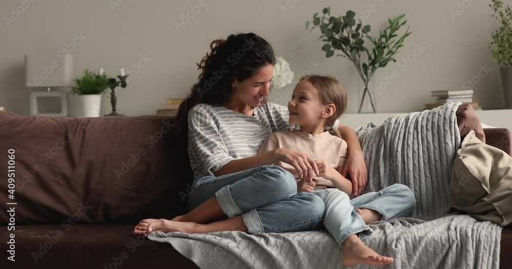 Young loving mother sitting on sofa at home talking to little preschool daughter, people enjoy confidential warm friendly conversation. Child upbringing, understanding and support, family bond concept Young loving mother sitting on sofa at home talking to little preschool daughter, people enjoy confidential warm friendly conversation. Child upbringing, understanding and support, family bond concept