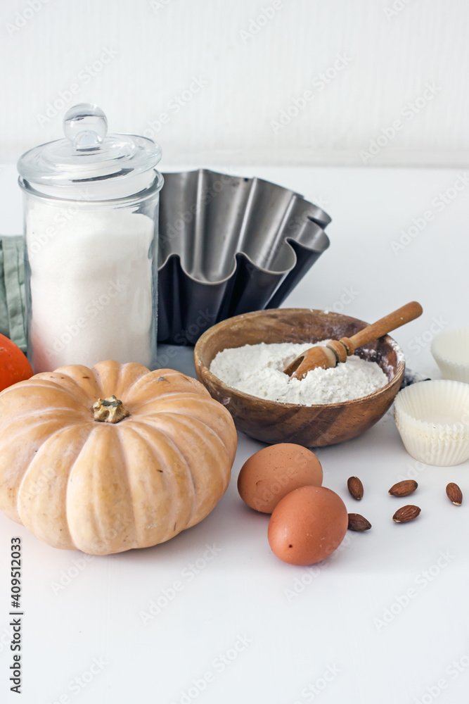 Ingredients for baking with pumpkin on a white table in the kitchen, flour, sugar, pumpkin, eggs, nuts, baking accessories, muffin molds. Home baker concept,authentic home hobby, cooking at home Ingredients for baking with pumpkin on a white table in the kitchen, flour, sugar, pumpkin, eggs, nuts, baking accessories, muffin molds. Home baker concept,authentic home hobby, cooking at home