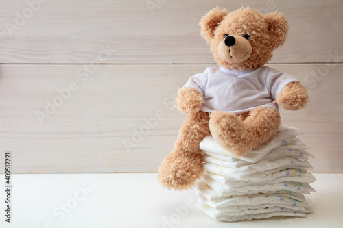 Baby diapers stack and teddy on white color floor photo