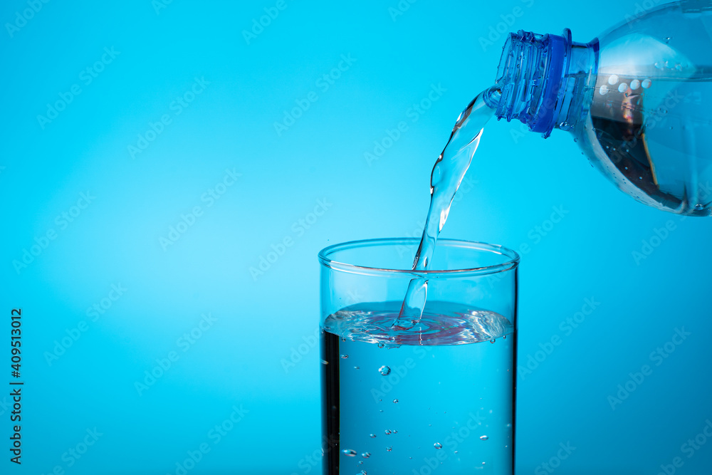 A glass filled with water from a plastic bottle on a blue background. Side view with copy space.