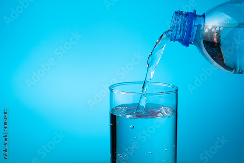 A glass filled with water from a plastic bottle on a blue background. Side view with copy space.