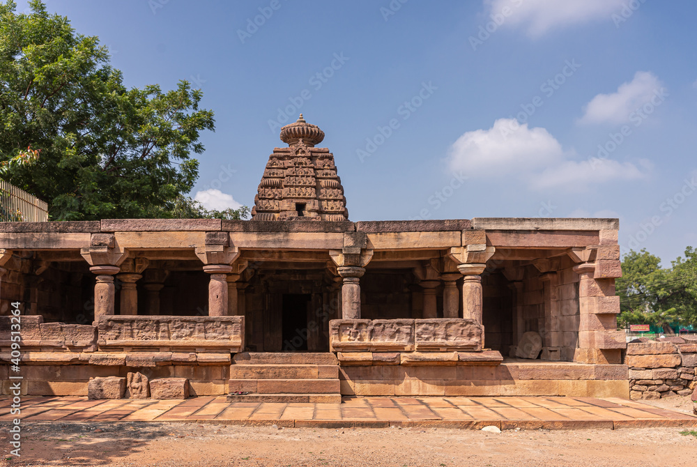 Aihole, Karnataka, India - November 7, 2013: Chakra Gudi temple building in brown stone under blue cloudscape and with green foliage on sides.