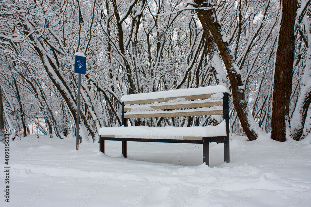 Horizontal subject conceptual photo with an empty bench in the snowy park with a sign 