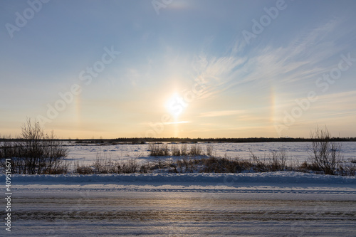 Snowy deserted road in winter on the orange a natural phenomenon halo glow background