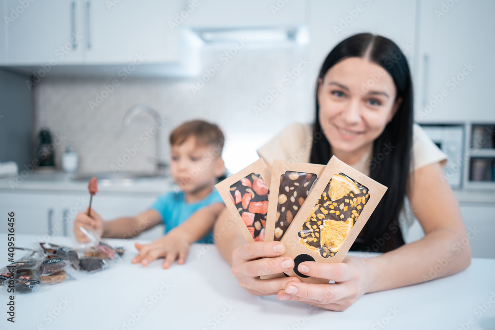 happy female and kid with handmade chocolate sweets or bars at home kitchen