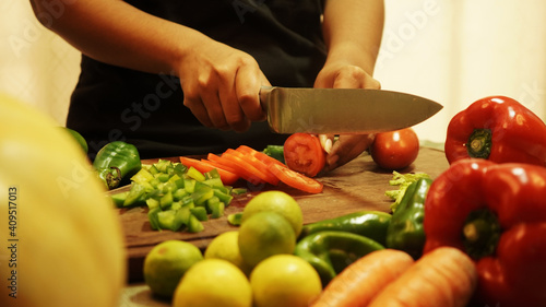 latin woman cutting vegetables in the kitchen with a knife and grabbing a vegetable, tomato, paprika, lemon and carrot